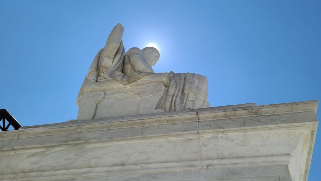 The sun creates a halo around the Authority of Law statue at the Supreme Court
