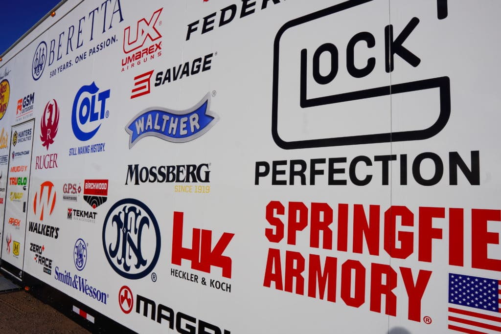 A collection of gun company logos appear on the side of a truck at SHOT Show 2022's range day