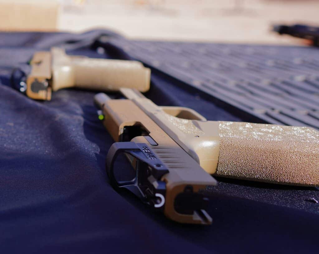 A handgun with an optic sight sits on a range table