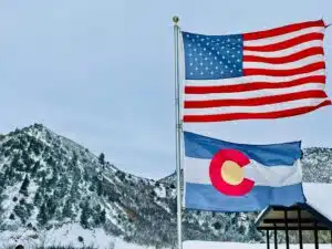 The American and Colorado flags flying in front of a mountain